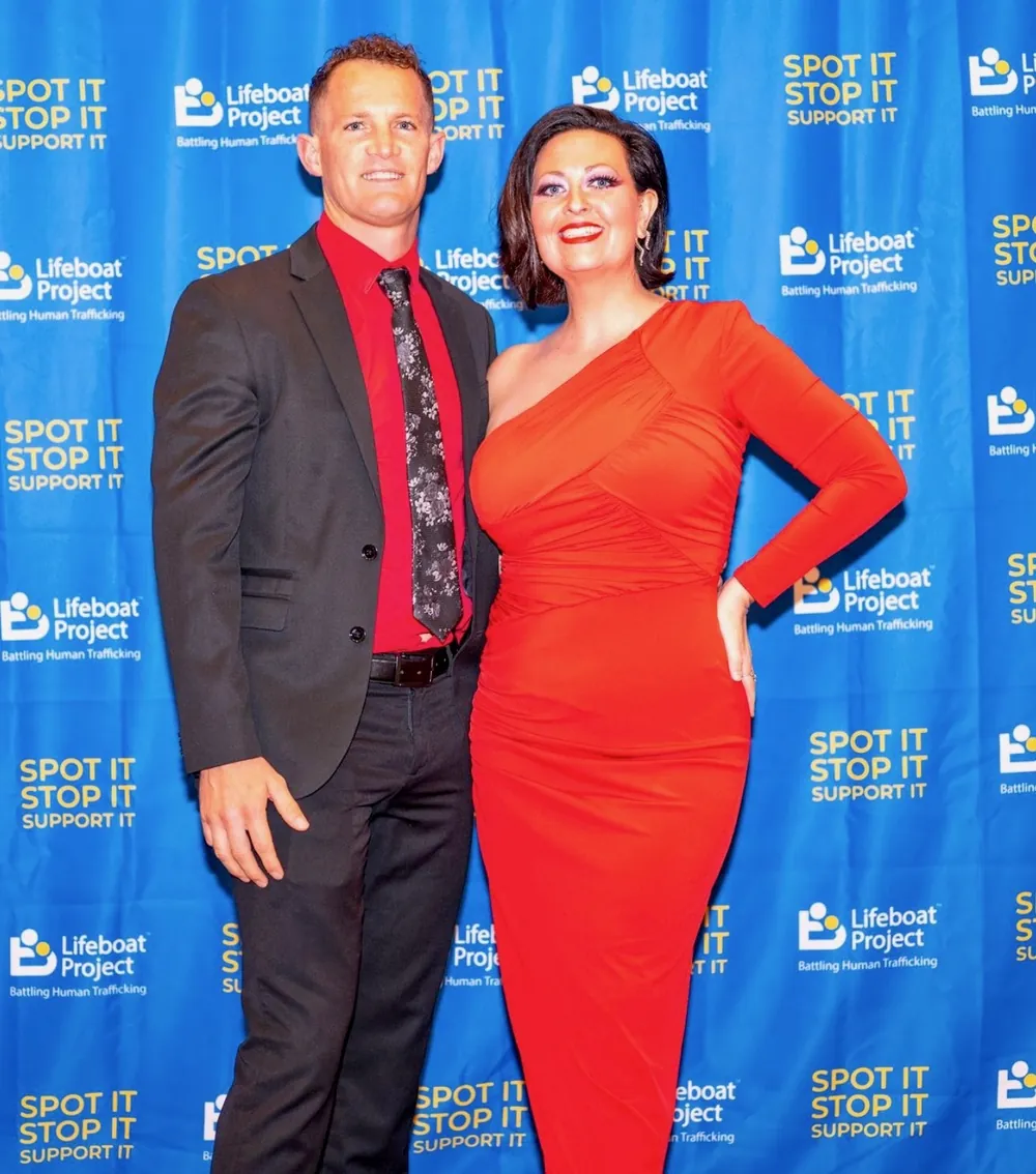 Guests in a dark suit and red dress pose together.