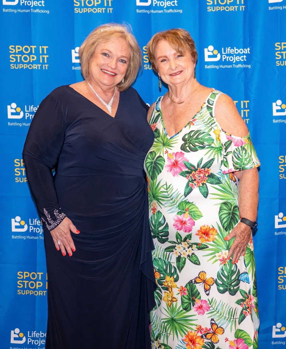 Two guests in black and floral dresses smile at the gala backdrop.