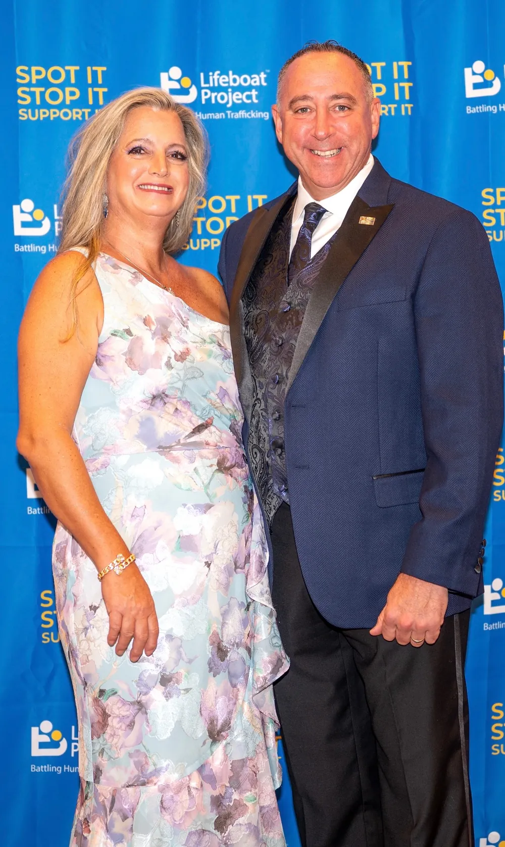 Guests in a floral dress and a suit with a red tie pose together.