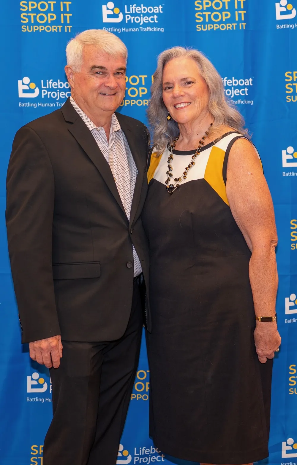 Two guests in a suit and blue dress pose at the gala backdrop.