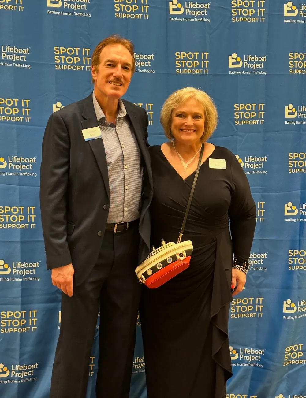 Two guests share a smile at the Lifeboat backdrop, with a sailboat purse.